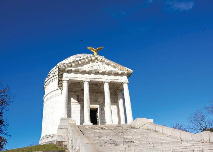 The Illinois Memorial at Vicksburg National Military Park, a white, cylinder-shaped structure with four large columns holding a small roof at the top of a steep, granite staircase. On the top of the roof, there is a golden eagle.