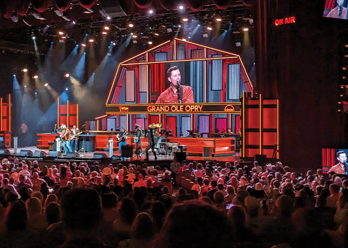 A live concert at the Grand Ole Opry in Nashville, where a male singer and his band performs in front of a large crowd of hundreds of people.