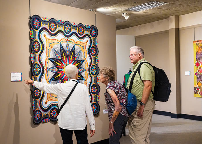 Three American Cruise Lines guests looking at a colorful quilt on display on the wall of the National Quilt Museum in Paducah. The guest on the left is pointing to the description of the artwork on the wall beside it.