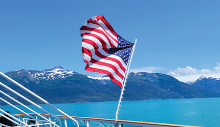 An American flag blowing in the breeze aboard a cruise through stunning snow-capped mountains.