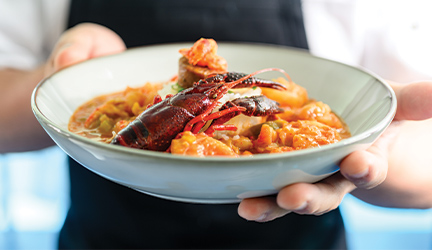 A close up view of a person holding a bowl of Crawfish Etouffee.