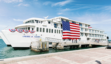 American Glory docked at a port with a large, vibrant American flag on its side.