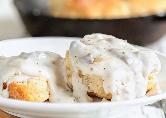 A plate of two biscuits with gravy smothered on top of each.