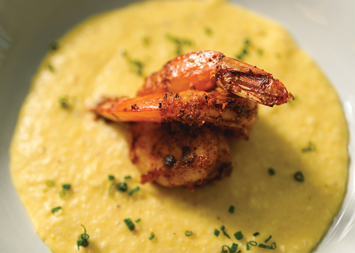 A bowl of soul food, made up of yellow colored grits topped with two large pieces of shrimp in the center of the bowl.