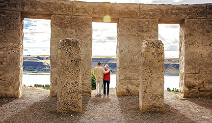 A couple stands together inside a Stonehenge structure, overlooking the Columbia River.
