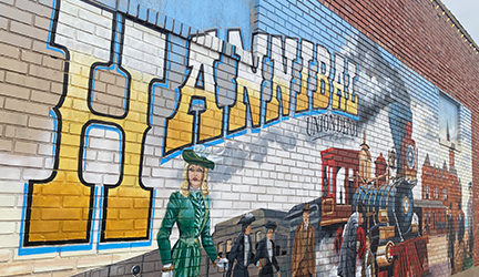 A striking mural on a building in Hannibal, Mississippi, featuring an artistic painting of the town name "Hannibal" beside a steam train on the wall.