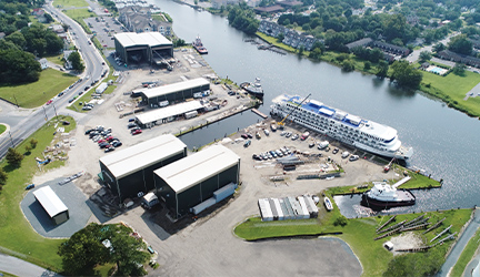 Aerial view of a river with a small cruise ship docked at an American shipbuilding facility.