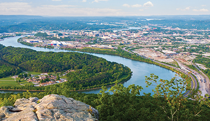 An aerial view of the Mississippi River, showcasing its bright blue winding waters, with sights of a large city in the distance.