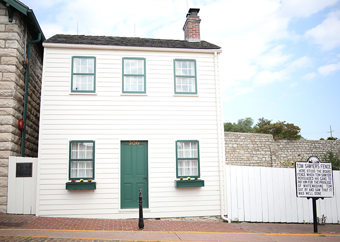 Mark Twain's light cream colored house with a dark green door and window planters in Hannibal, to the left of the whitewashed fence of Tom Sawyer.