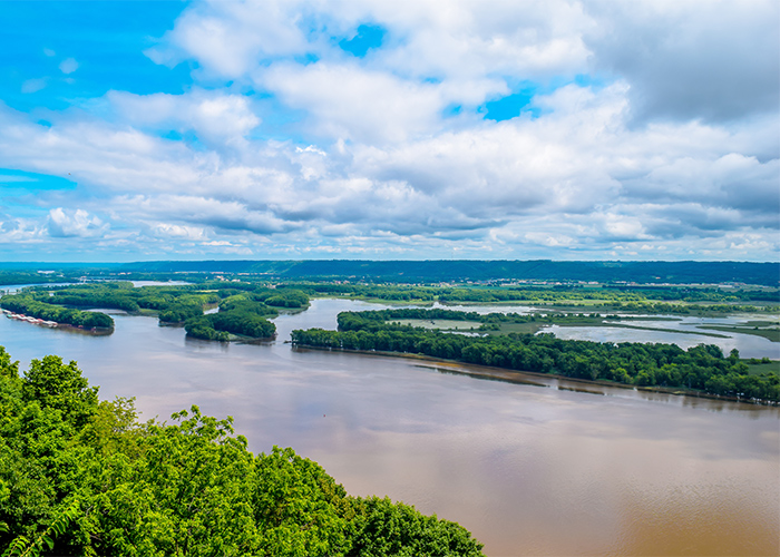 An aerial view of the Mississippi River, with several grass inlets, and an outline of mountains in the distance.