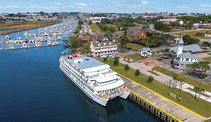 A Southeast U.S. cruise ship docked at a marina, surrounded by boats and a quaint town with historic buildings and a lighthouse.