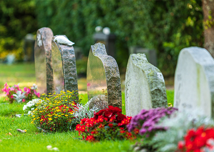 Five gravestones in a line beside each other in Historic Natchez Cemetery. In front of each headstone, there are colorful, planted flowers.