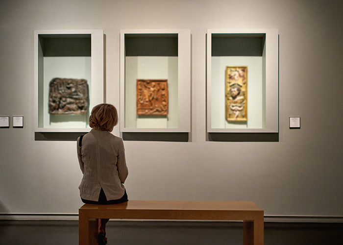 A woman sitting on a wooden bench admiring three historic artifacts in white frames on the wall at Martha’s Vineyard Museum.