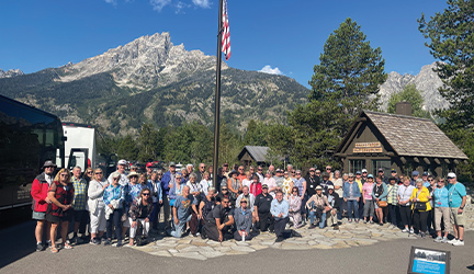 A large group of cruise guests photographed surrounding an American flag in front of a large mountain