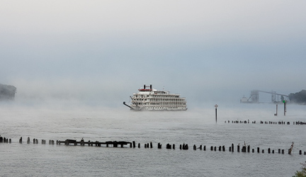 An small cruise ship sailing through dense fog, setting a spooky scene. 