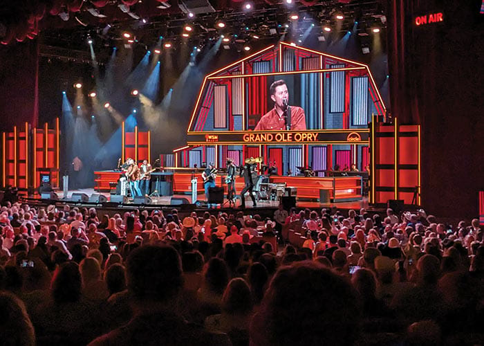 A live concert at the Grand Ole Opry in Nashville, where a male singer and his band performs in front of a large crowd of hundreds of people.