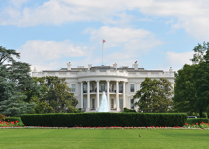 The White House with a fountain and gardens, under a blue sky with clouds.