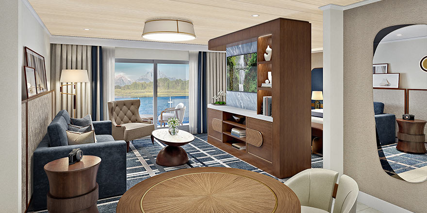 The Grand Suite on American Encore, with large floor-to-ceiling sliding glass doors leading to a private balcony overlooking the Columbia River. There is a navy blue sofa and a tan armchair facing a large wooden TV stand in the center of the room, with a TV and shelves with decor. 