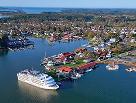 An aerial view of American Constitution, an American Cruise Lines small cruise ship docked in St. Michaels along the Chesapeake Bay with trees and buildings filling the shore.