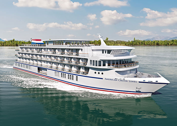 An aerial view of American Maverick, an American Cruise Lines Patriot Class small cruise ship sailing along the New England coast, with views of the shore in the distance.