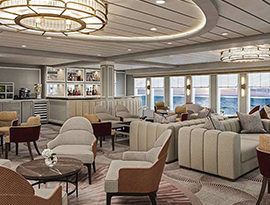 The Chesapeake Lounge, a common area on American Ranger, with two tan sofas, several lounge chairs and small round tables, and a small bar in the back corner. The right wall is filled with large windows overlooking the sunset on the Hudson River.