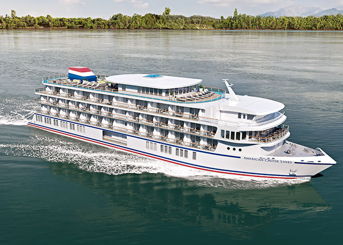 An aerial view of American Ranger, an American Cruise Lines Patriot Class small cruise ship sailing along the Hudson River, with views of the shore in the distance.