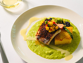 A white dinner plate with Blackened Florida Grouper, Caramelized Polenta Cake, Cilantro Lime Grits, Mango Pico de Gallo, and Champagne Butter Sauce, served by American Cruise Lines.